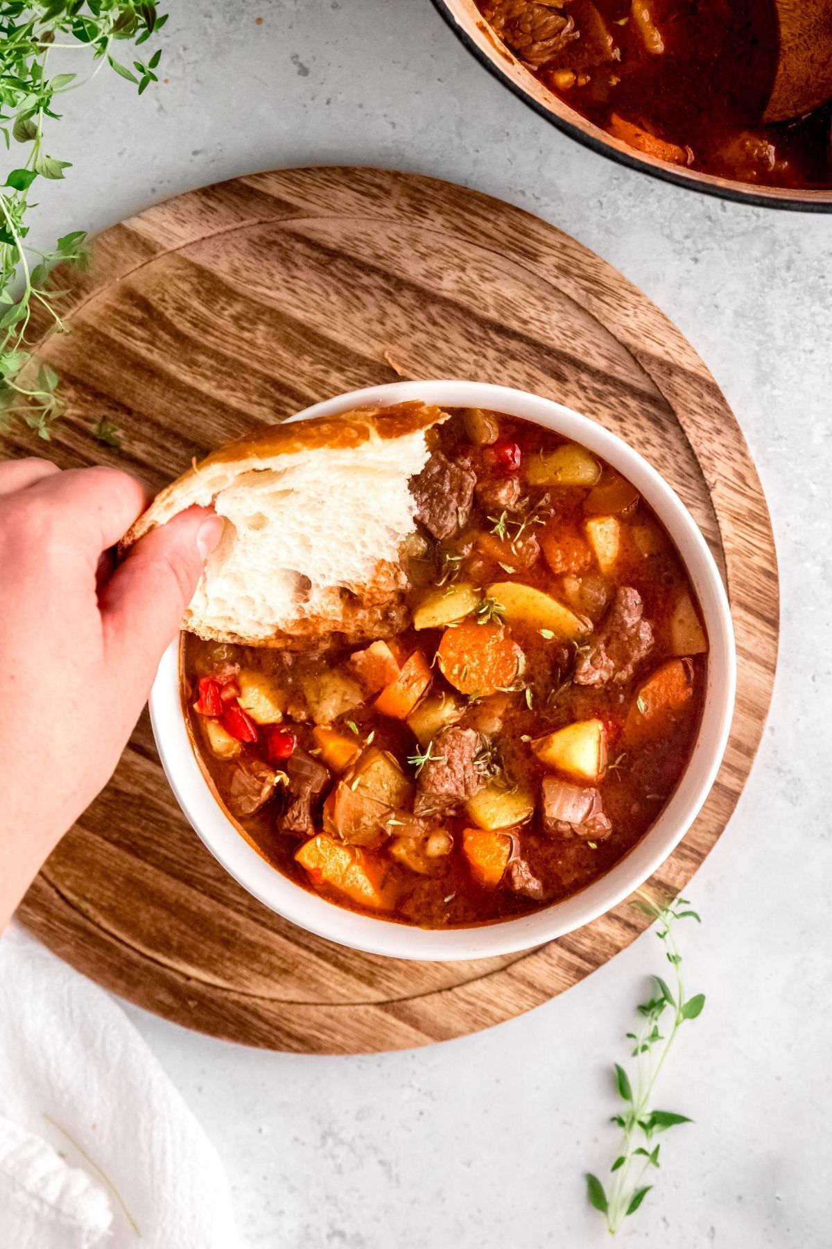 hand dunking a slice of crusty bread into the Dutch Oven Beef Stew.