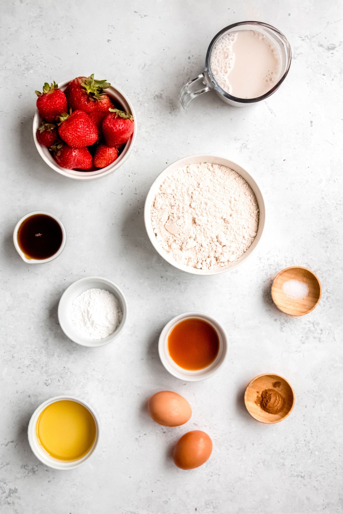 flat lay shot of the ingredients needed to make healthy strawberry waffles measured out into bowls on a white table.