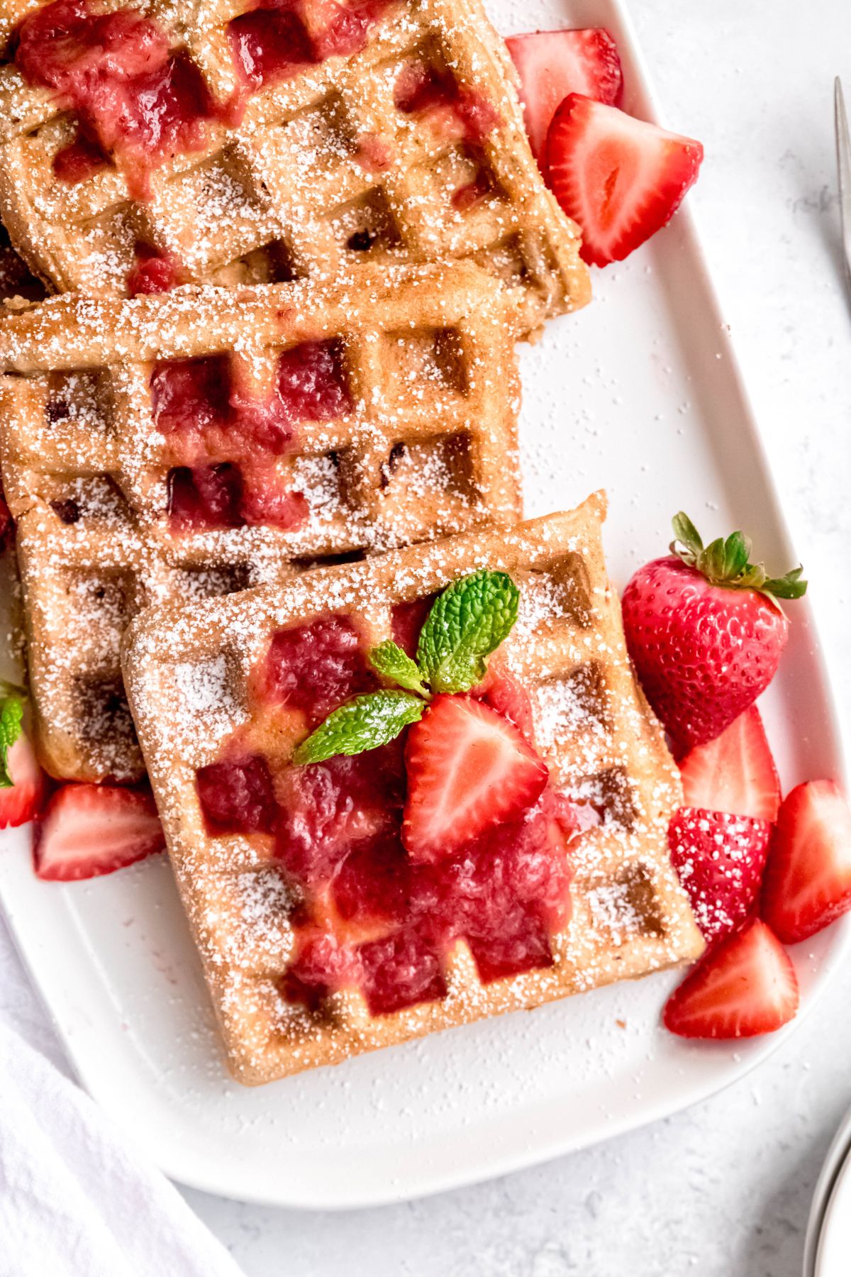hero shot of whole-grain, refined sugar-free strawberry waffles on a white plate.