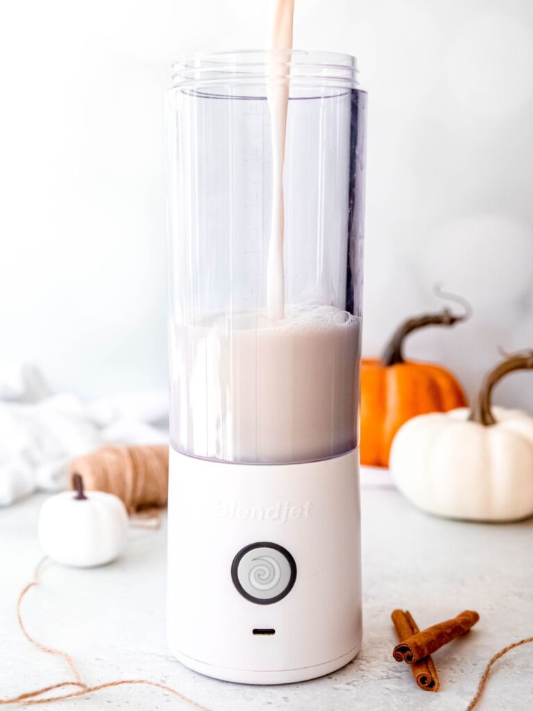 action shot of pouring almond milk into a portable blender.