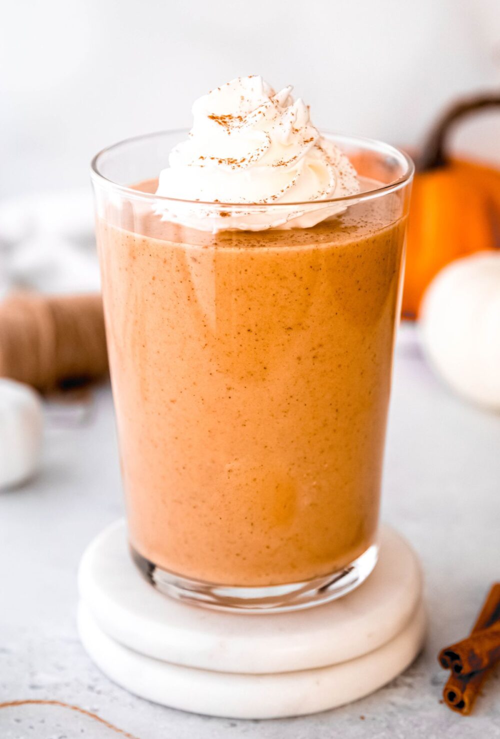 hero image of a pumpkin protein smoothie on a white coaster on a table with mini pumpkins and whole spices.