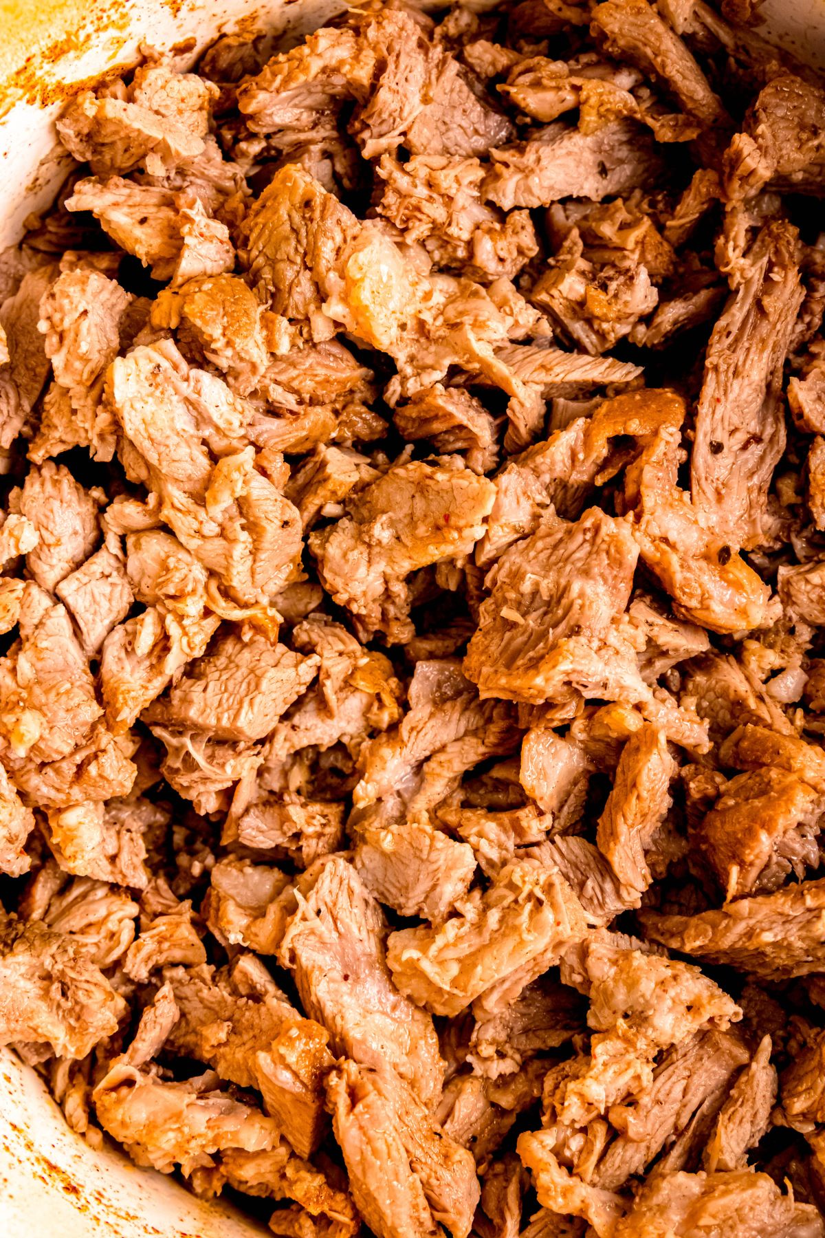hyper closeup flatlay shot of Mexican pork carnitas in a Dutch oven after being shredded.