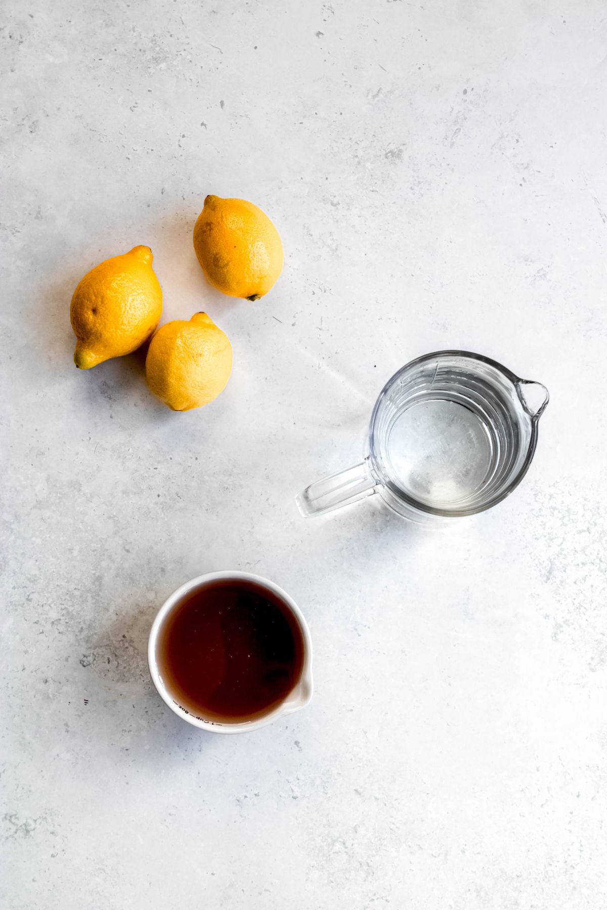 flat lay shot of fresh lemons, a pitcher of water, and a ramekin of lavender simple syrup for making lavender lemonade.