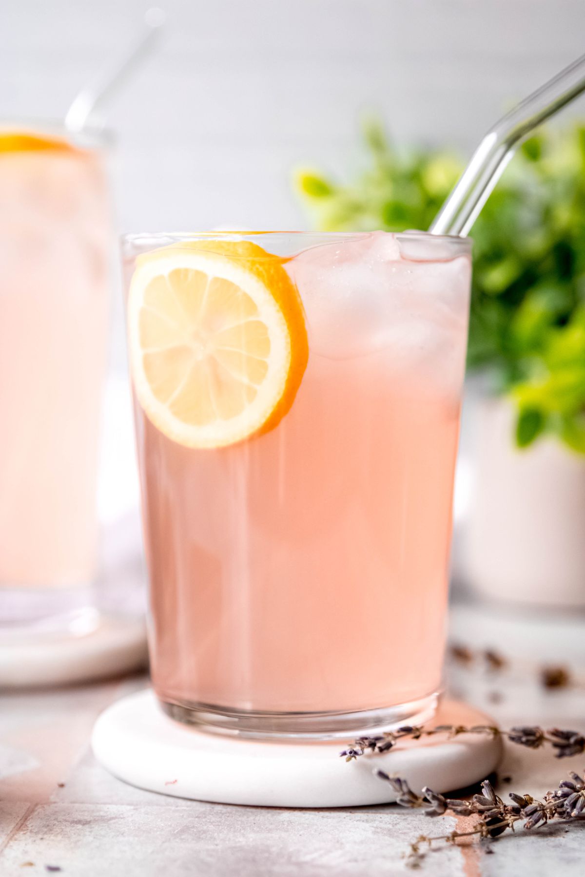 glass of lavender-sweetened lemonade in a clear glass with a glass straw and a slice of lemon.
