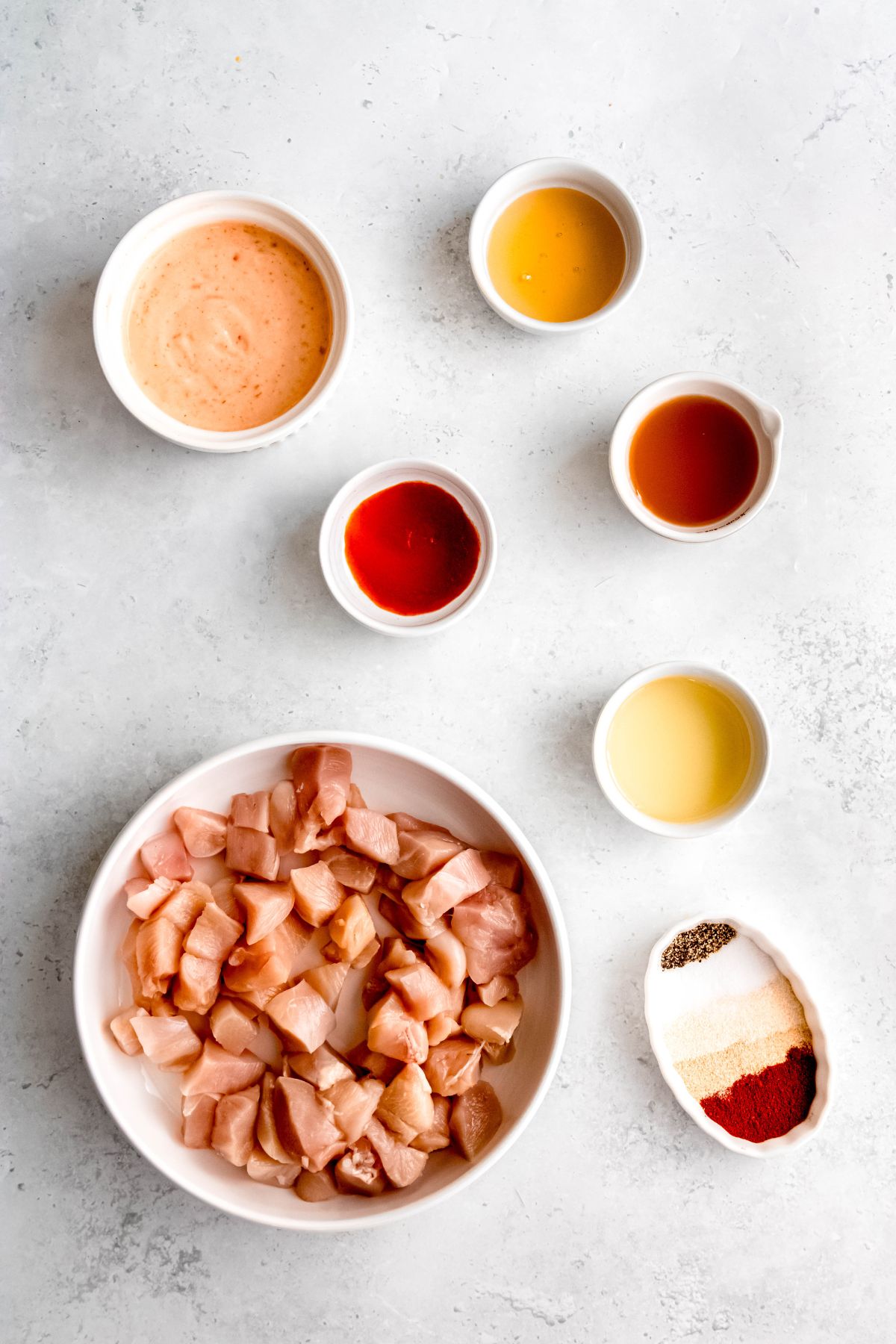 ingredients for making homemade Bonefish Grill inspired bang bang chicken skewers measured out into bowls on a white table.