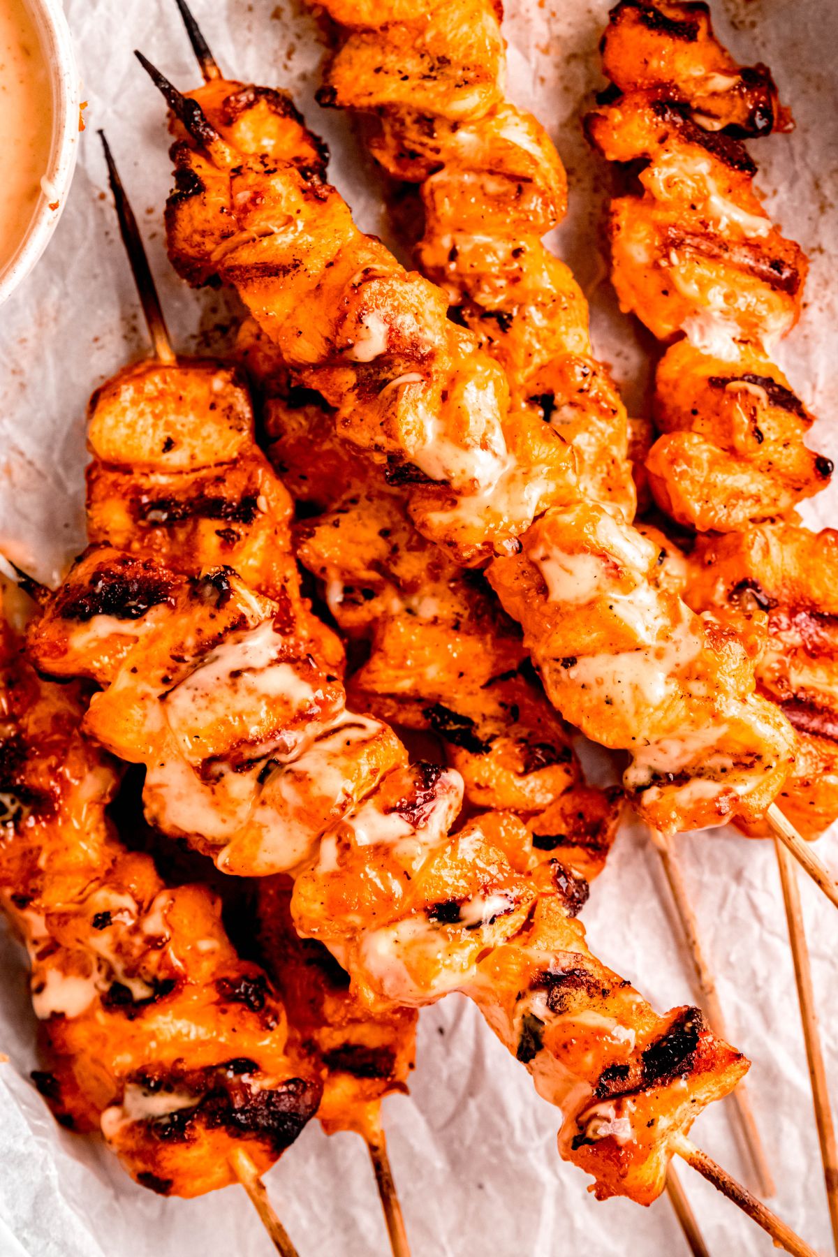 stack of grilled bang bang chicken skewers on a piece of crumpled parchment with a side of extra bang bang sauce for dipping.