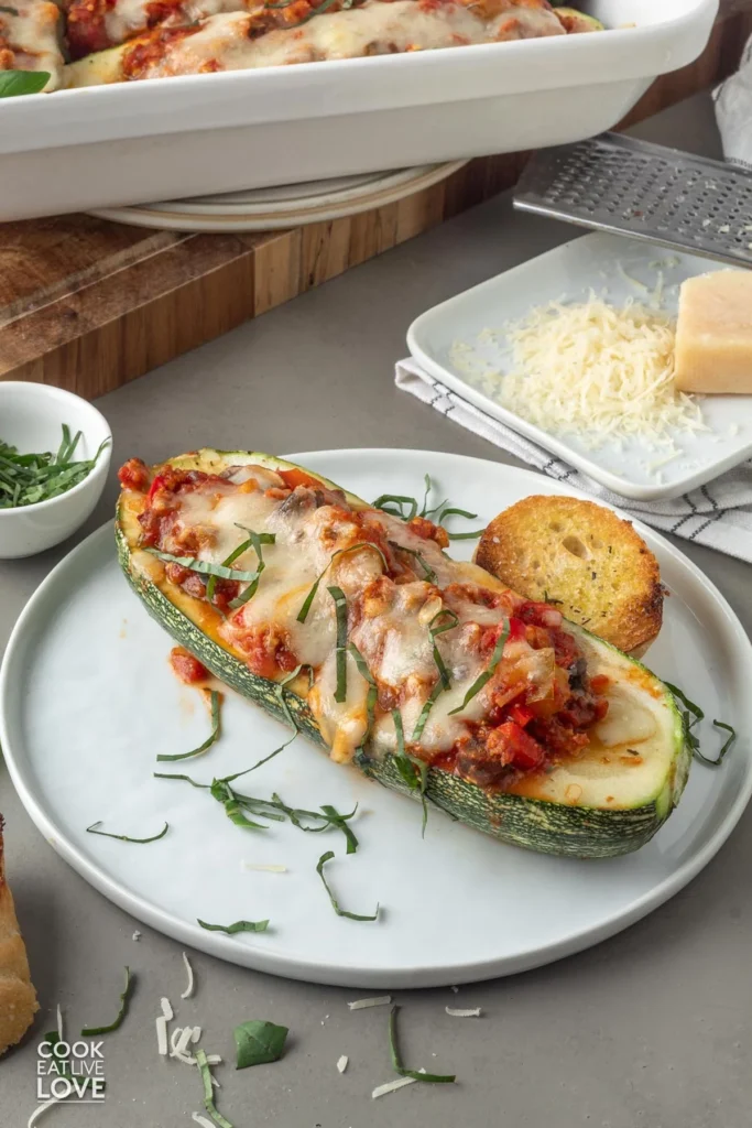 A vegetarian-stuffed zucchini boat on a plate with chiffonade basil on top.