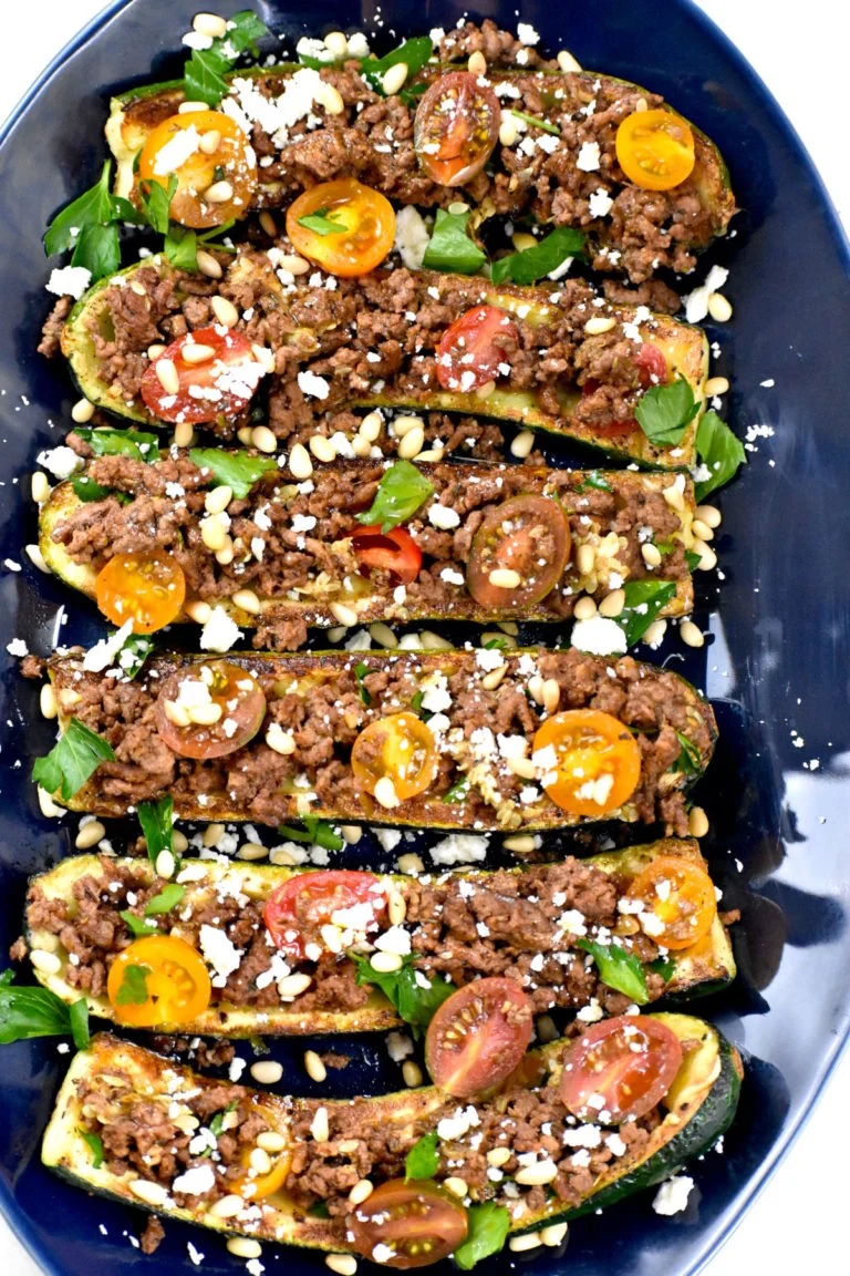 An overhead shot of a dark blue plate of mediterranean zucchini boats.