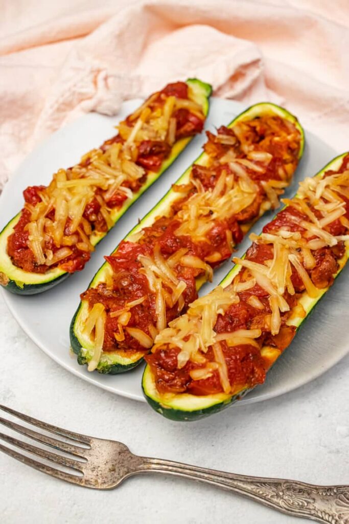 Three vegan stuffed zucchini boats on a dinner plate with a fork.