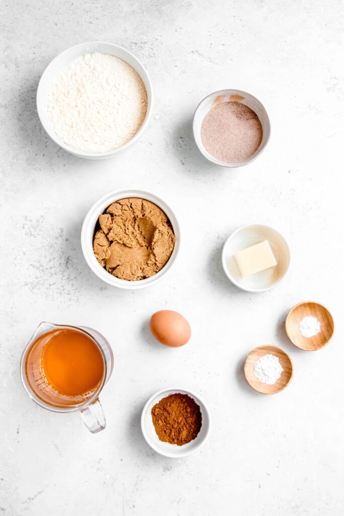 ingredients needed to make apple cider cookies measured out into bowls on a white table.