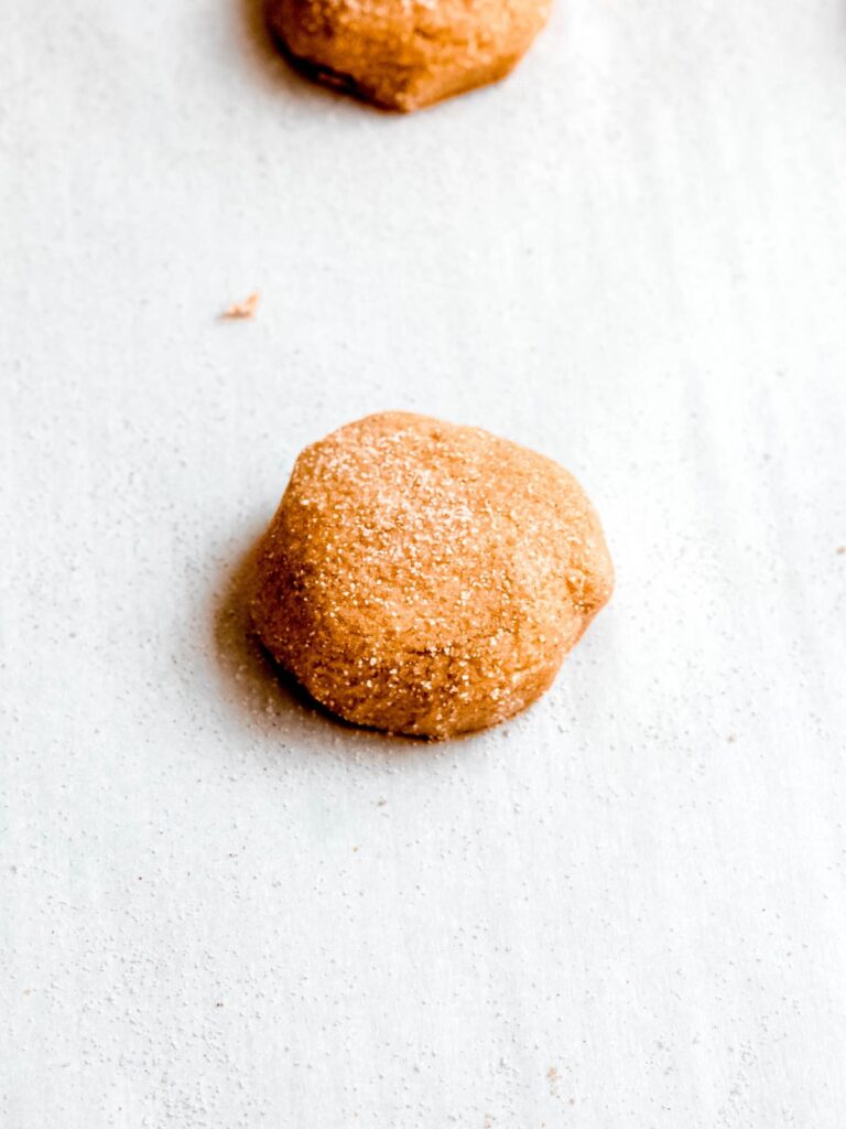 small, slightly flattened ball of raw apple cookie dough on a parchment lined sheet after rolling in cinnamon sugar.