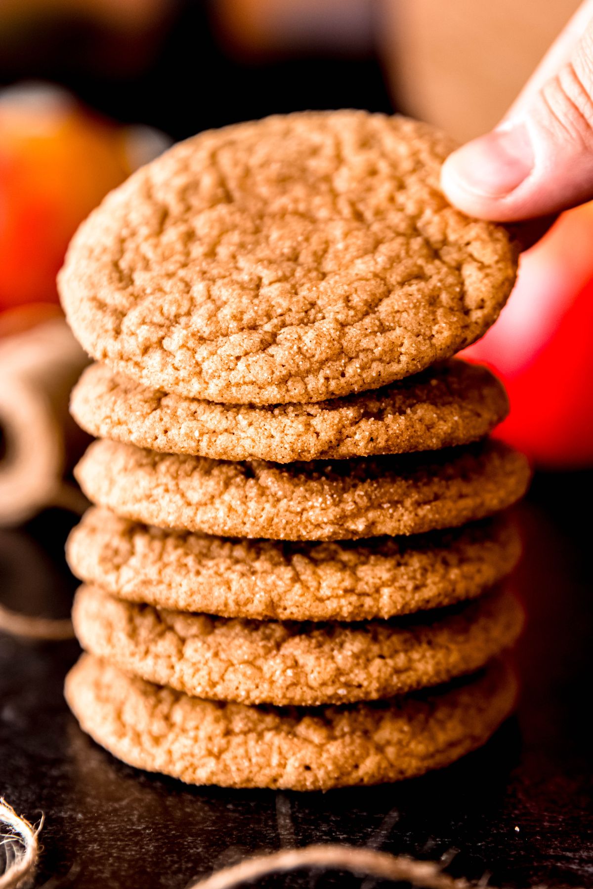 hand taking the top apple cider cookie from a stack of 6 on a black table with natural twine and whole apples around.