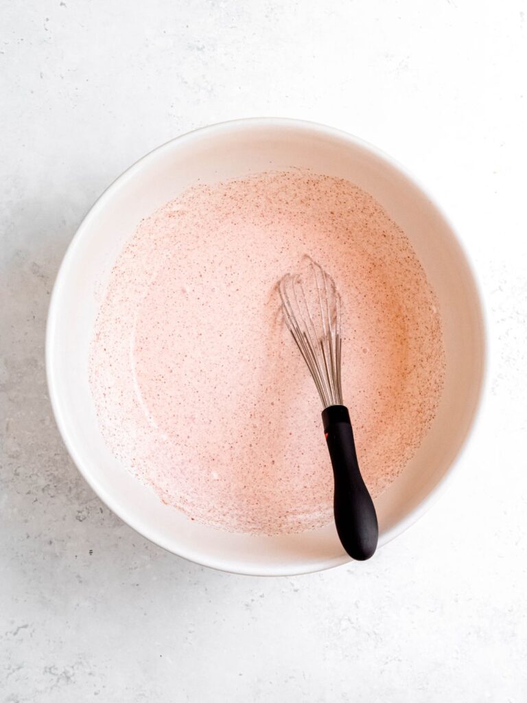 small whisk in a white mixing bowl with the street corn salad dressing.