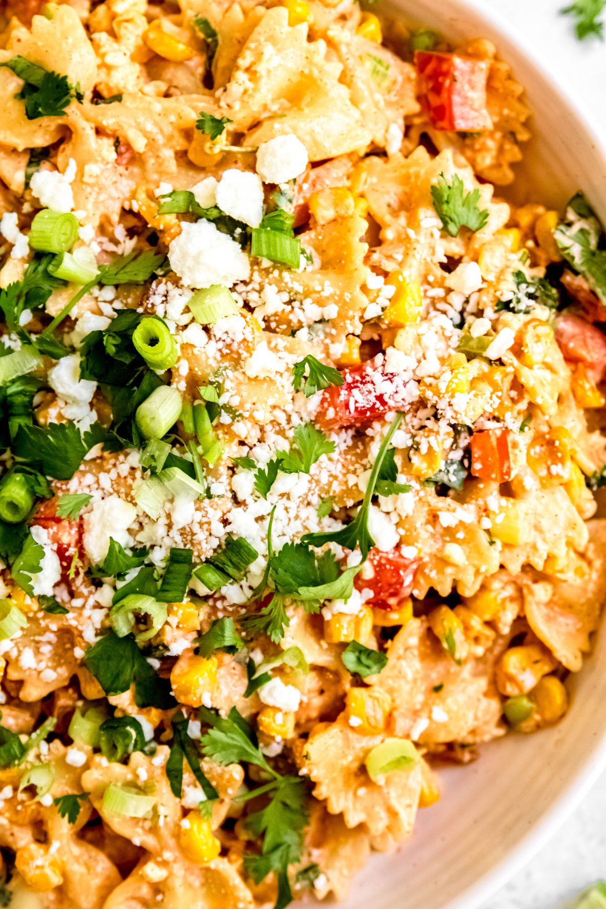flat lay closeup of a serving bowl of elote street corn pasta salad topped with white cotija cheese crumbles, chopped scallions and fresh cilantro.