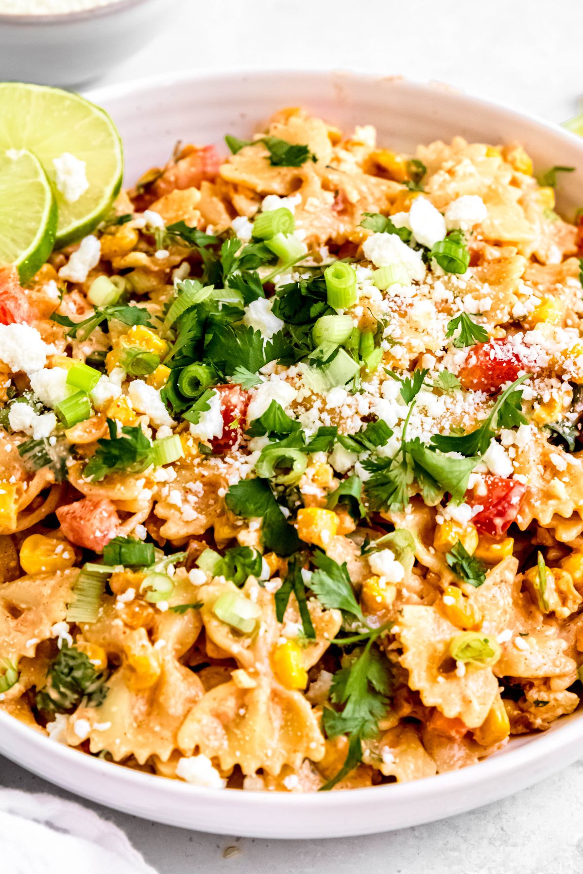45 degree angle shot of a serving bowl of roasted Mexican corn pasta salad garnished with cheese, fresh cilantro, and chopped green onions.