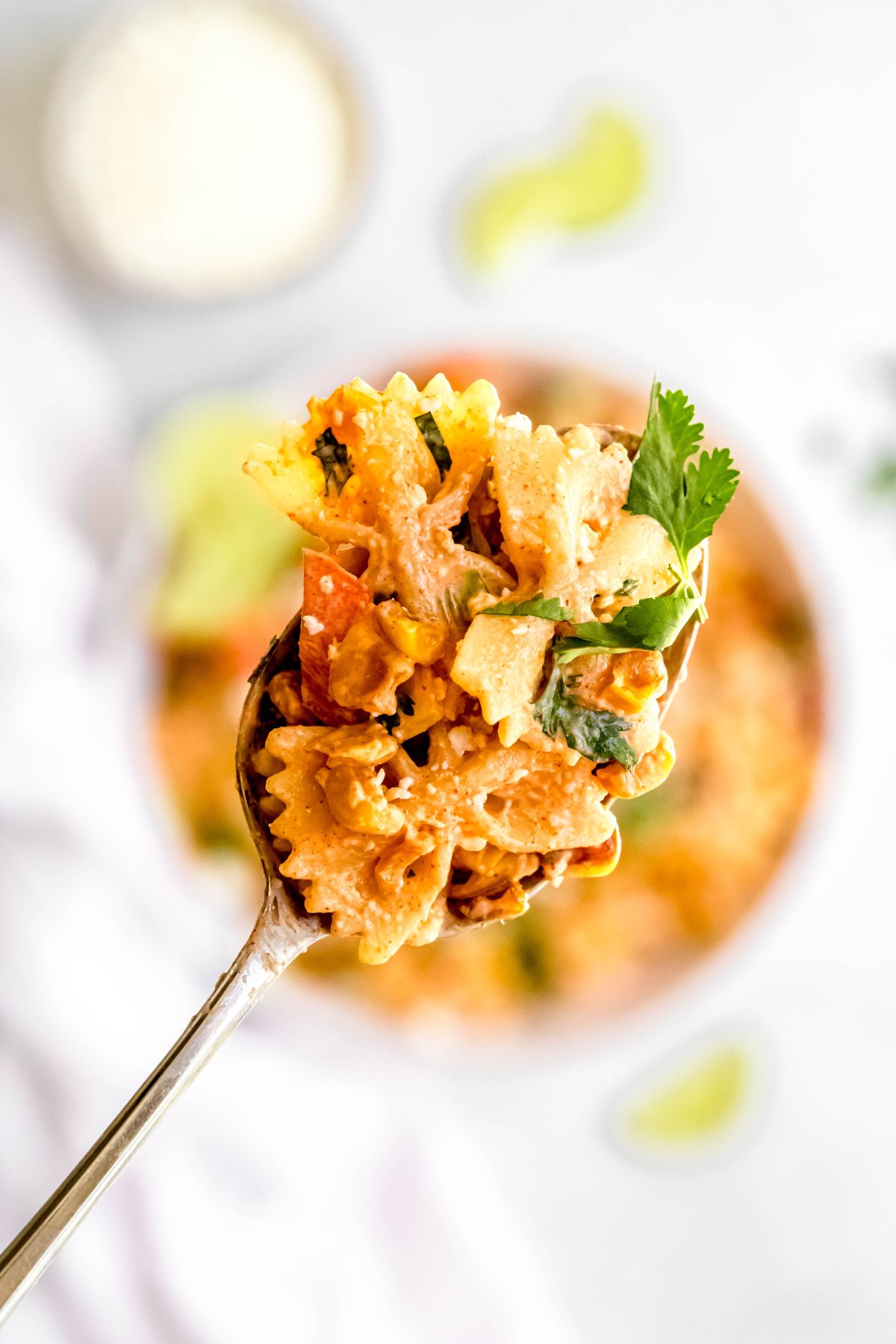 silver serving spoonful of roasted corn pasta salad with the rest of the serving bowl blurred out below.