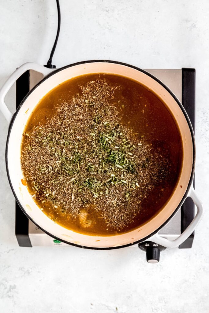 fresh and dried herbs floating on top of the broth in the Dutch oven.