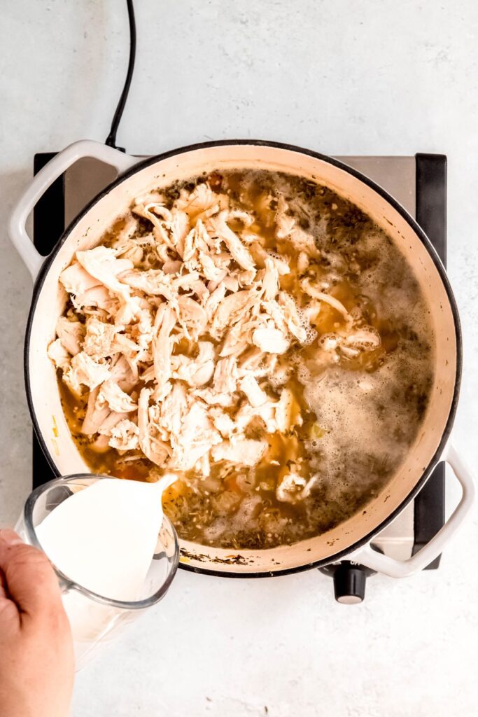 action shot of cream being poured into the soup pot with the shredded turkey on top.