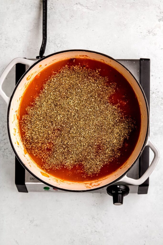A Dutch oven with crushed tomatoes and seasonings.