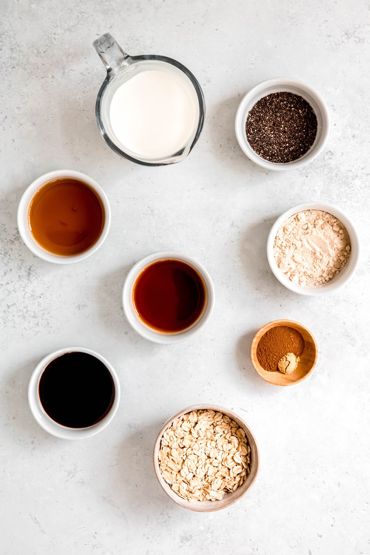 flat lay shot of ingredients needed to make high protein gingerbread overnight oats with protein powder measured out into bowls on a white table.