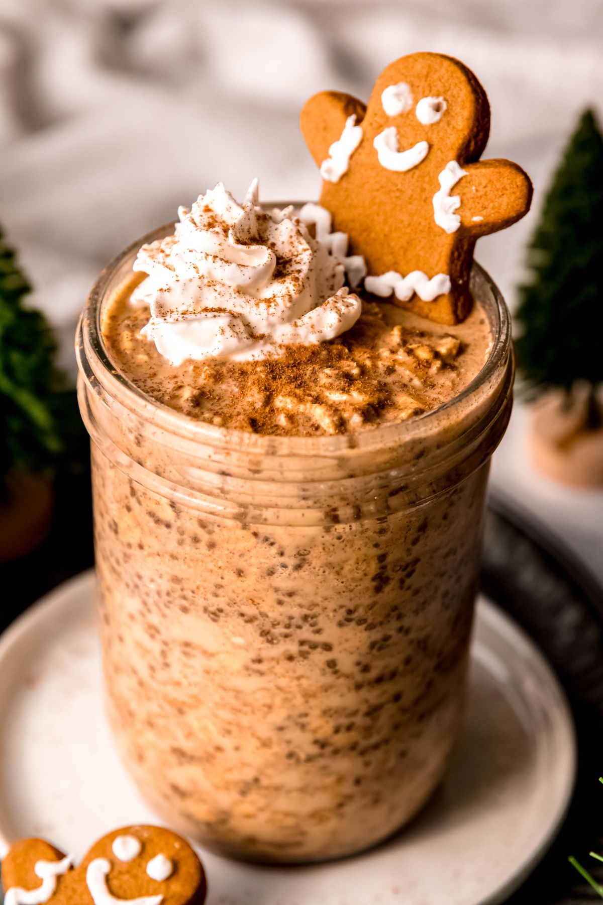 clear pint-sized wide-mouth mason jar filled with high protein gingerbread overnight oats topped with a squirt of whipped cream, a mini gingerbreadman cookie, and a sprinkle of cinnamon.