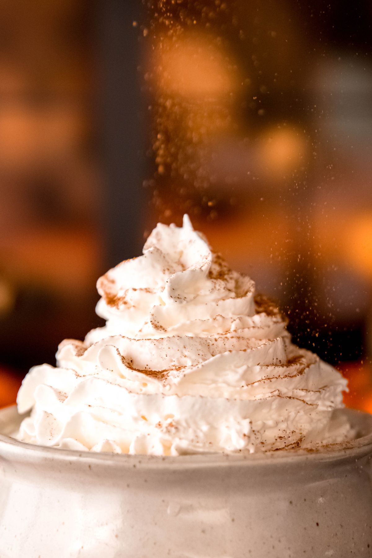 action shot of homemade pumpkin spice being sprinkled atop whipped cream in an earthenware mug filled with coffee.