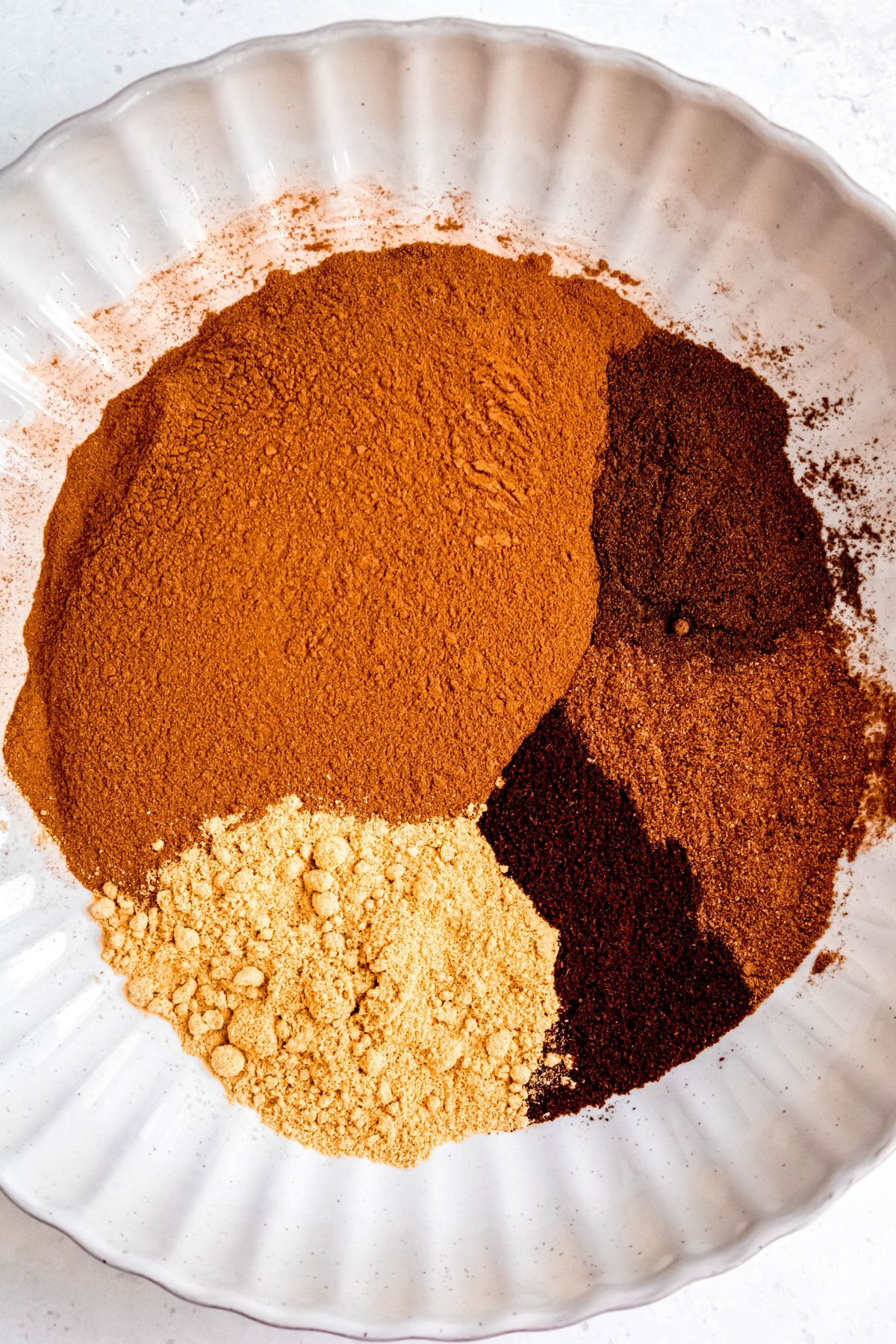 white scalloped bowl with piles of ground cinnamon, ginger, allspice, nutmeg and ginger before stirring.
