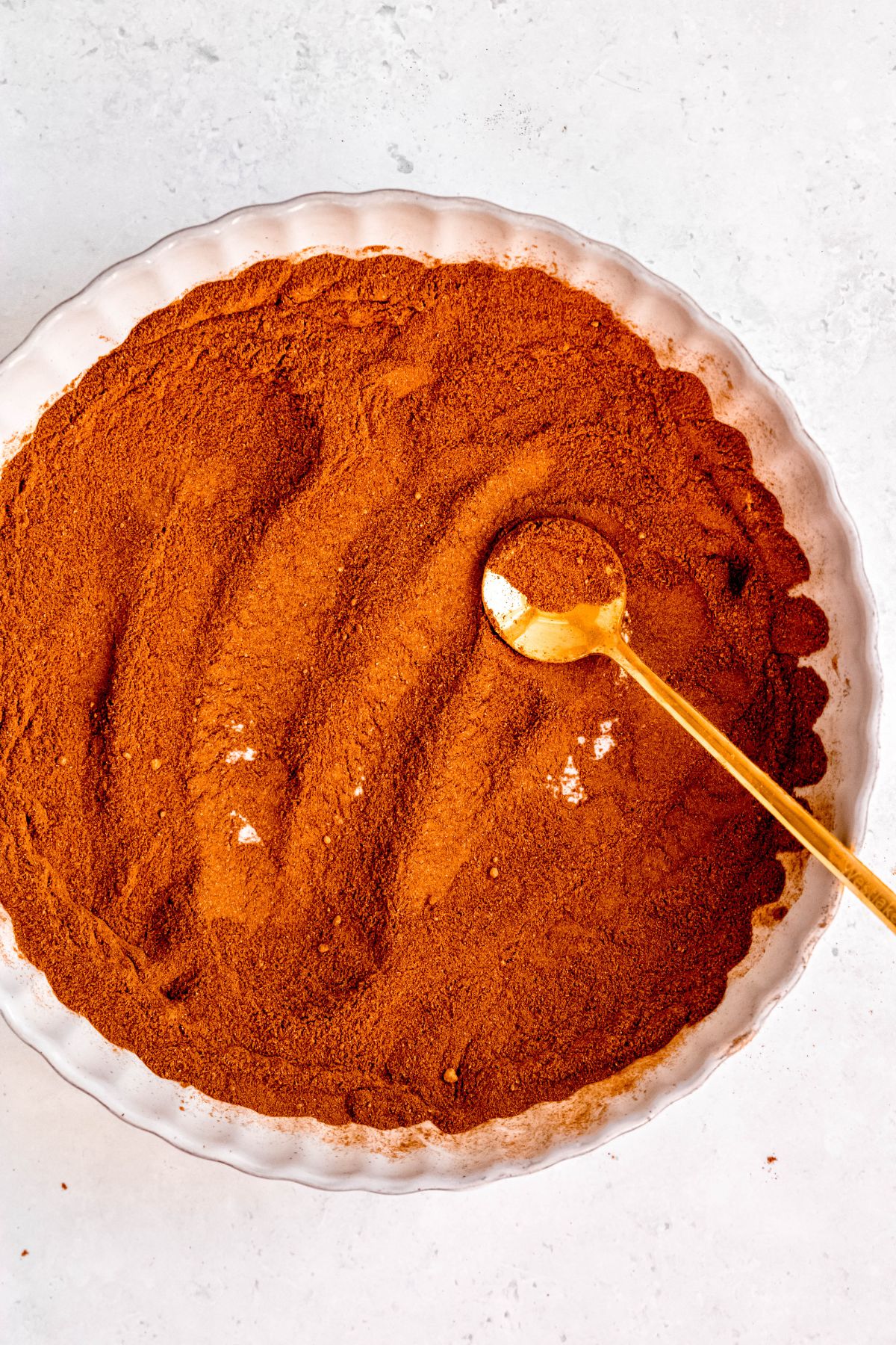 pumpkin pie spice blend in the bowl with a gold soup spoon after mixing together; it's a warm orange brown color.