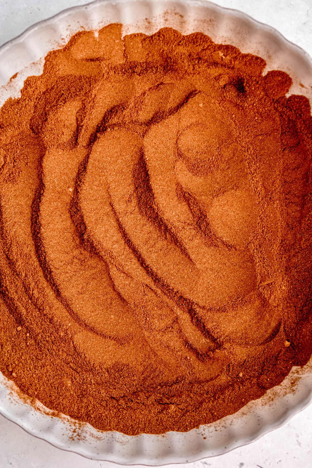 round scalloped white ramekin filled with homemade pumpkin pie spice mix with spoon marks dragged through the top.