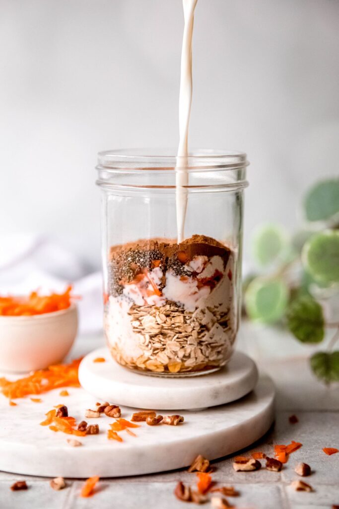 action shot of the milk being poured into the mason jar with the oats and flavorings to make carrot cake overnight oats.