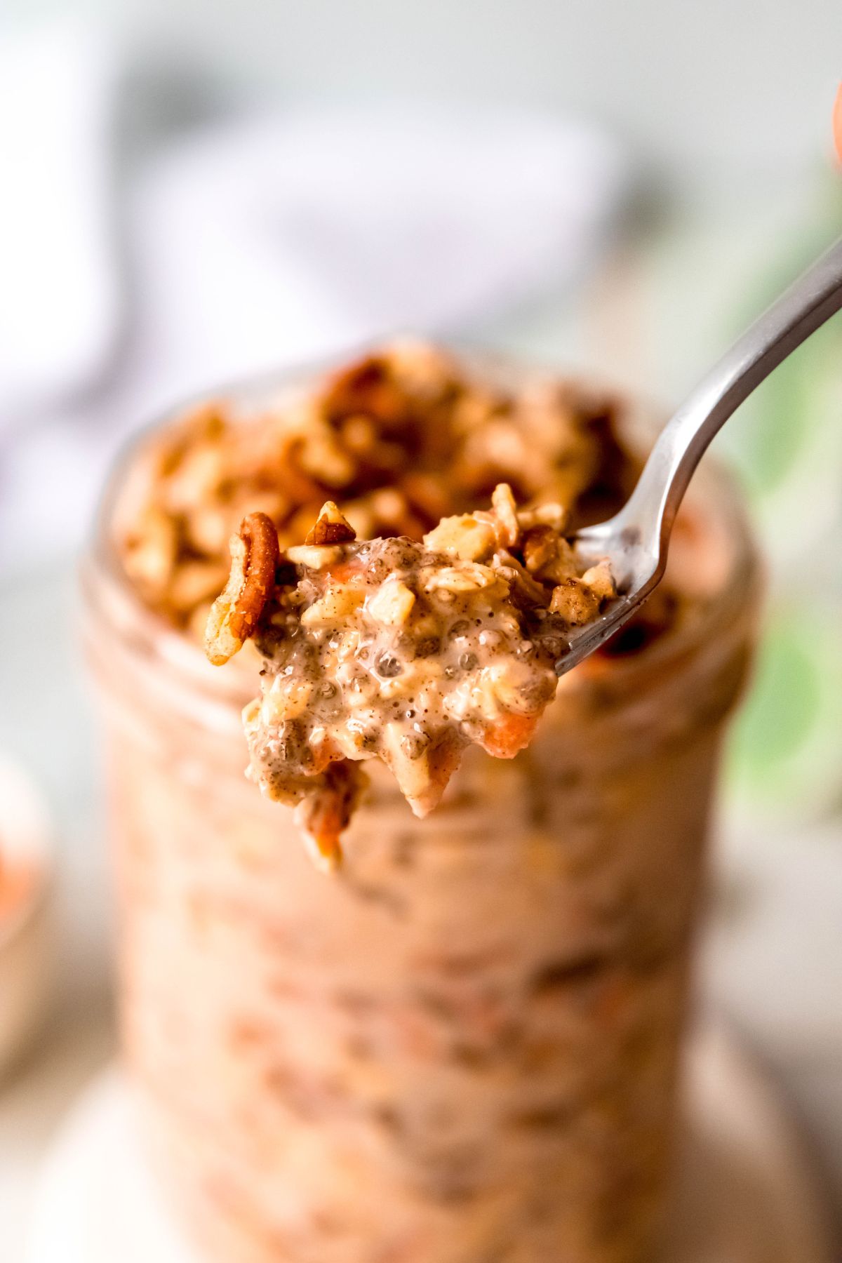 closeup shot of a spoonful of protein-packed carrot cake over night oats in front of the rest of the jar that is blurred out in the background.