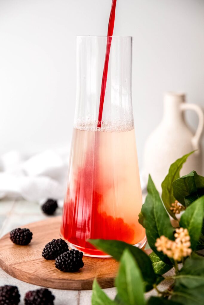 action shot of blackberry syrup being poured into the pitcher with the lemon water mixture.