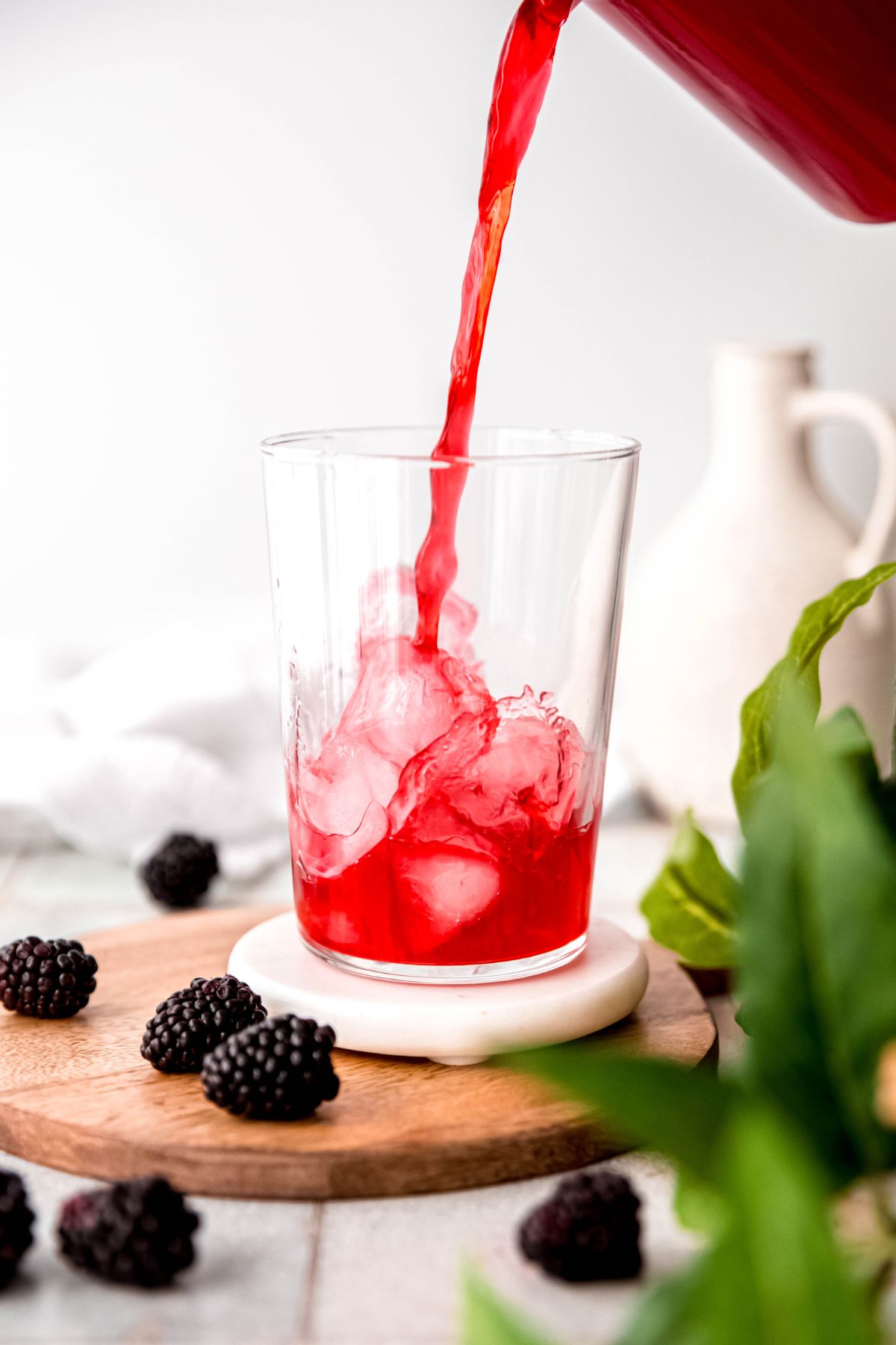 action shot of blackberry lemonade being poured over a glass of ice.