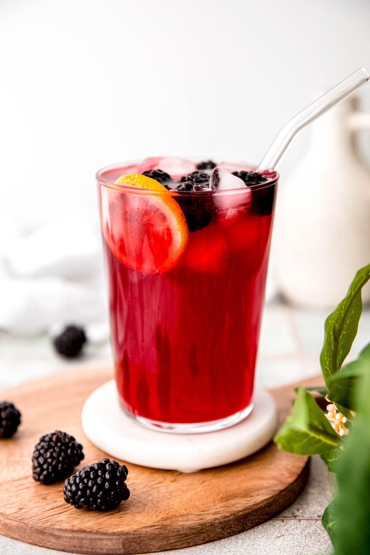 clear glass filled with bright red blackberry lemonade topped with a lemon wheel, fresh berries, and a glass straw.