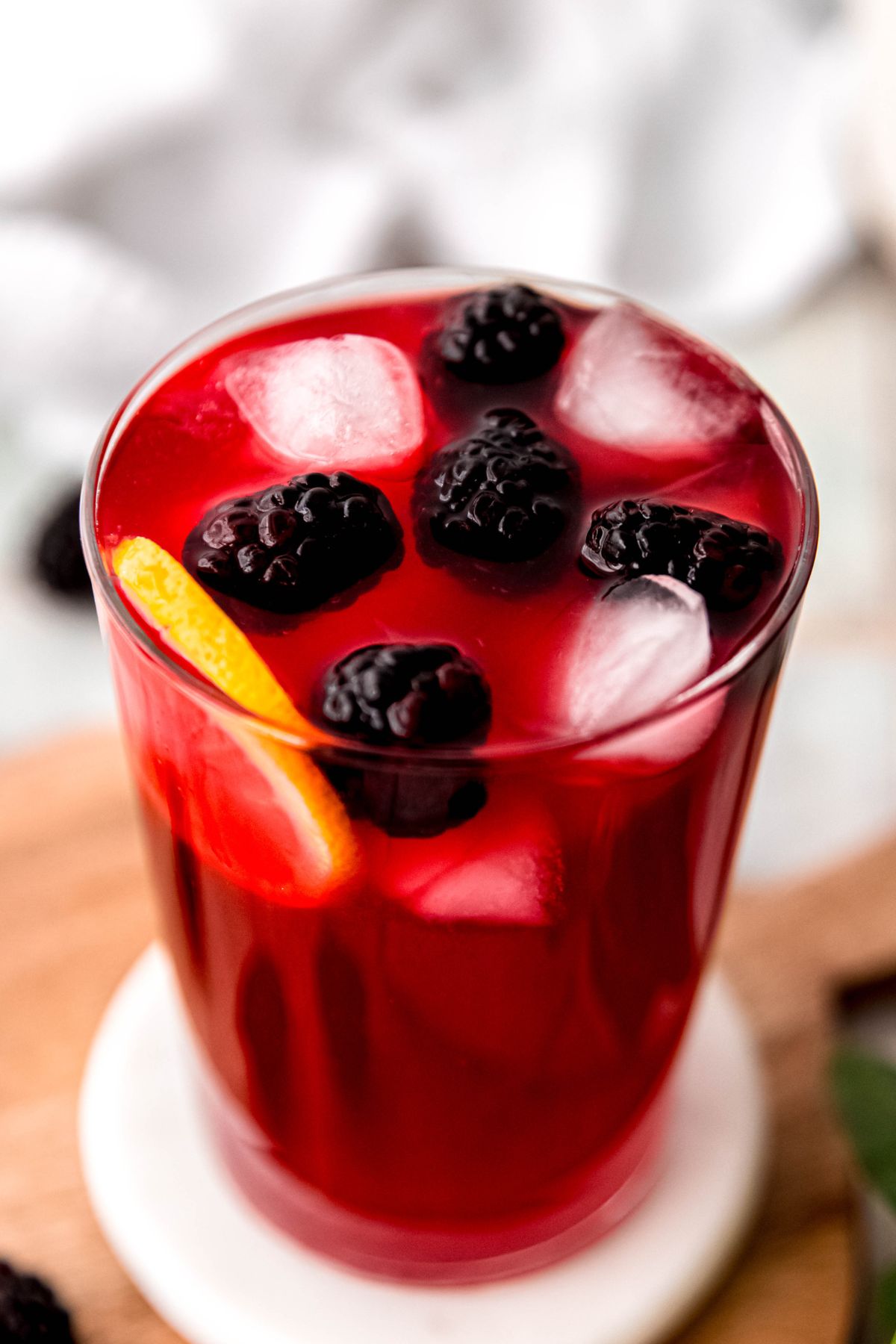 closeup 45 degree angle shot of a glass of blackberry lemonade showing the ice, fresh blackberries, and lemon wheel floating at the top.