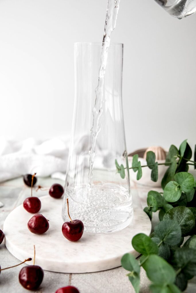 action shot of water being poured into a clear glass pitcher without a handle.