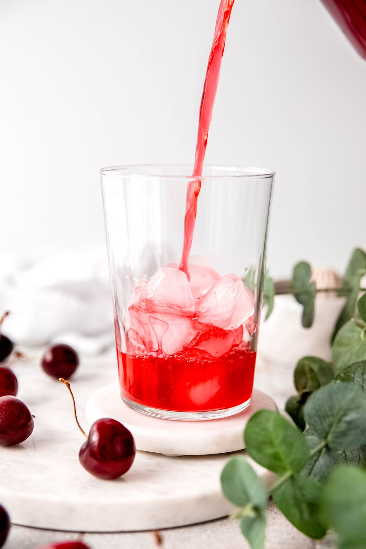 action shot of homemade cherry lemonade being poured into a clear pint glass with ice.