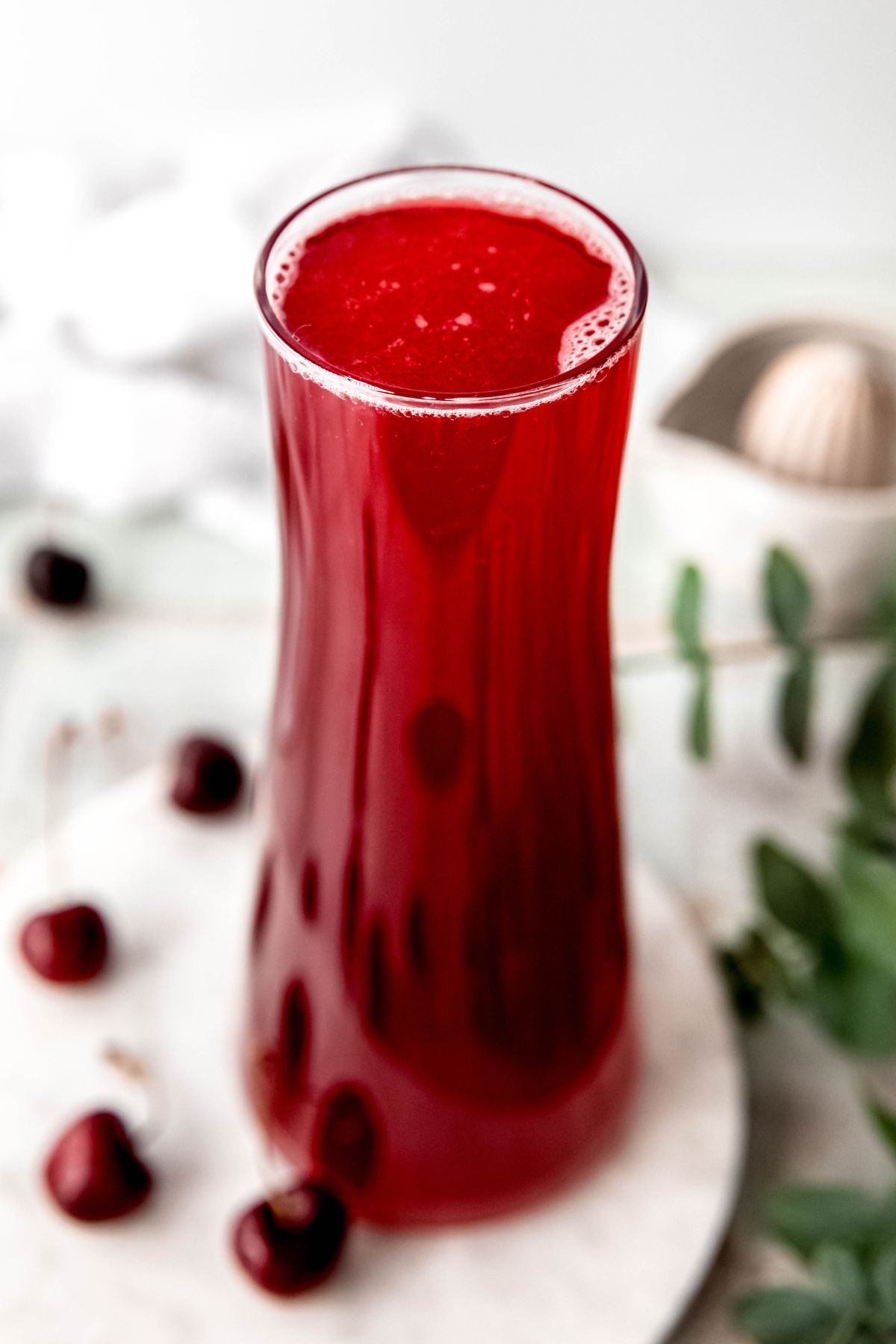 tall hourglass shaped clear glass pitcher filled with a batch of homemade cherry lemonade recipe.