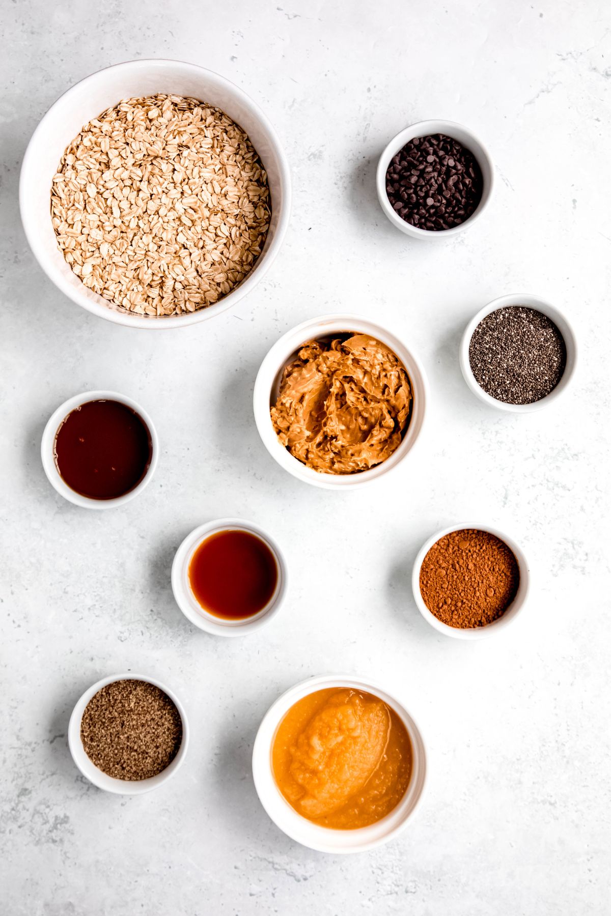 overhead shot of the ingredients needed to make oatmeal chocolate chip protein cookies measured out into white bowls on a white table.