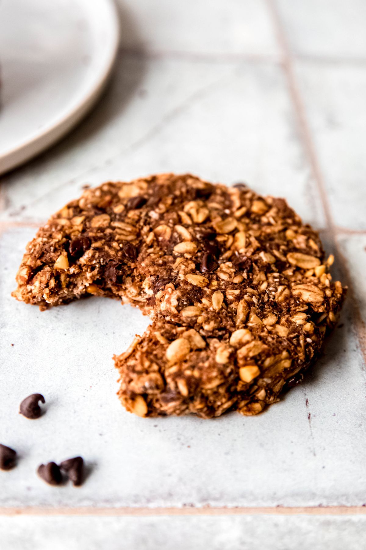 single chocolate chocolate chip oatmeal protein cookie on a grey slate table with a bite taken out.