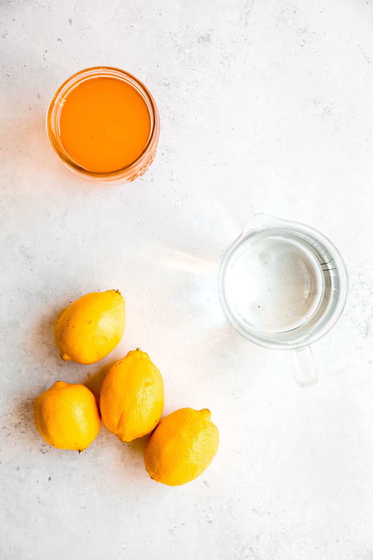 fresh lemons, water, and homemade peach syrup measured out for making peach-flavored lemonade.