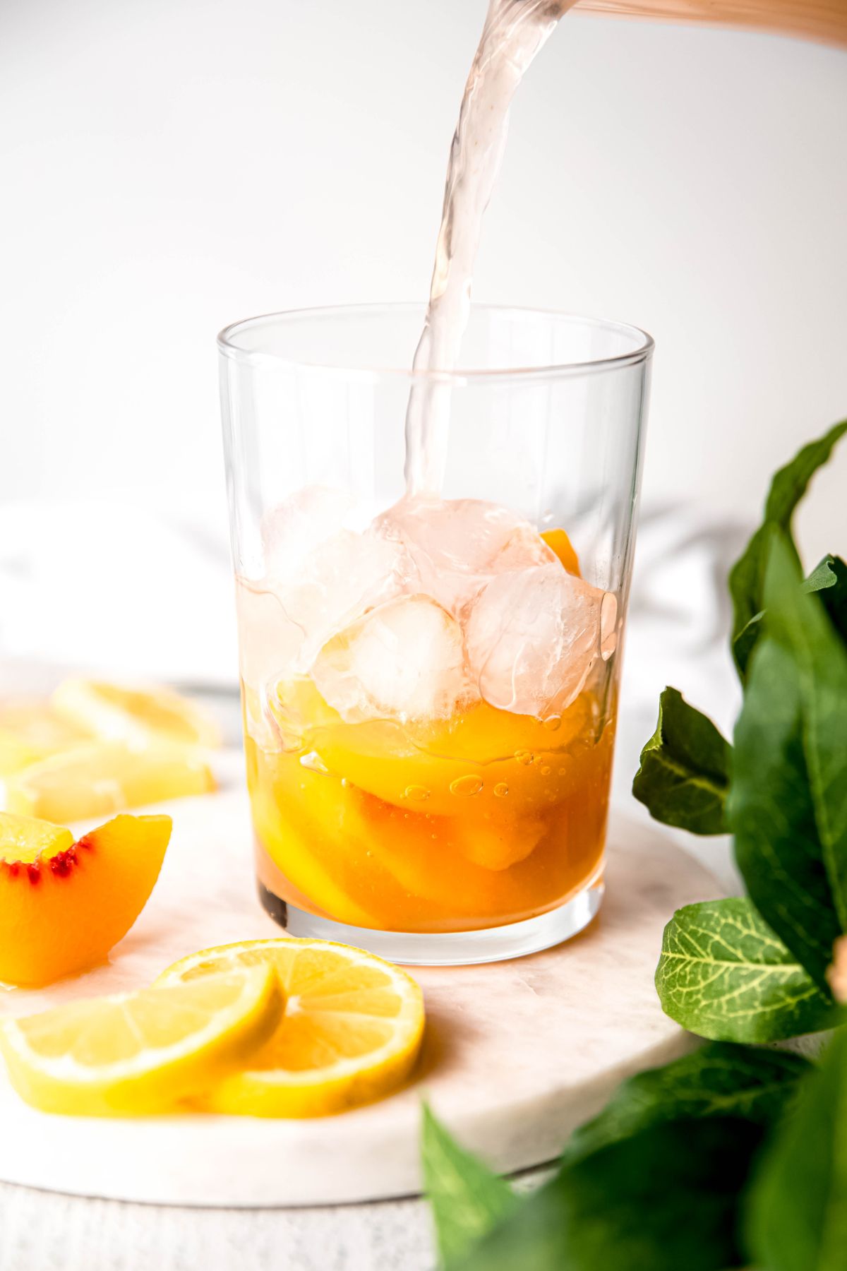 peach lemonade being poured over a glass of ice and frozen peaches to serve.