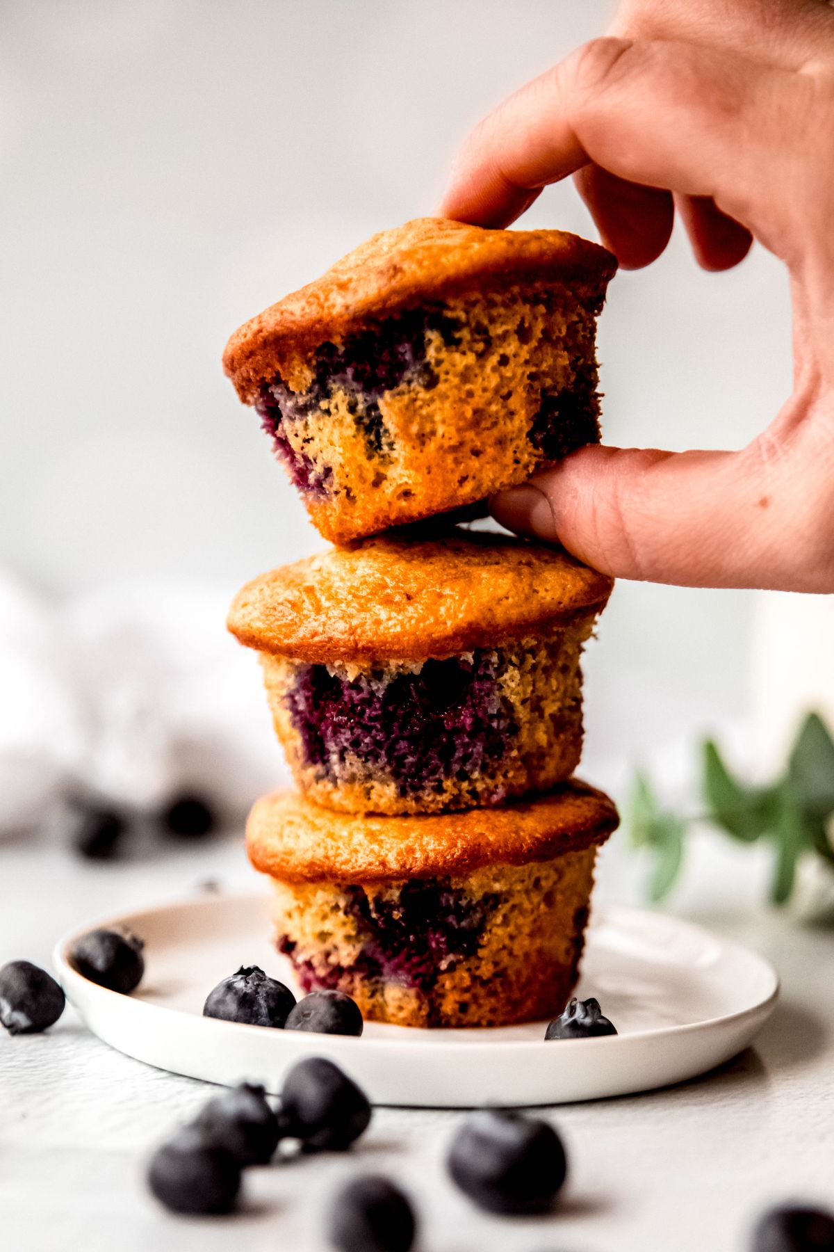A hand grabbing a protein blueberry muffin from the top of a stack.