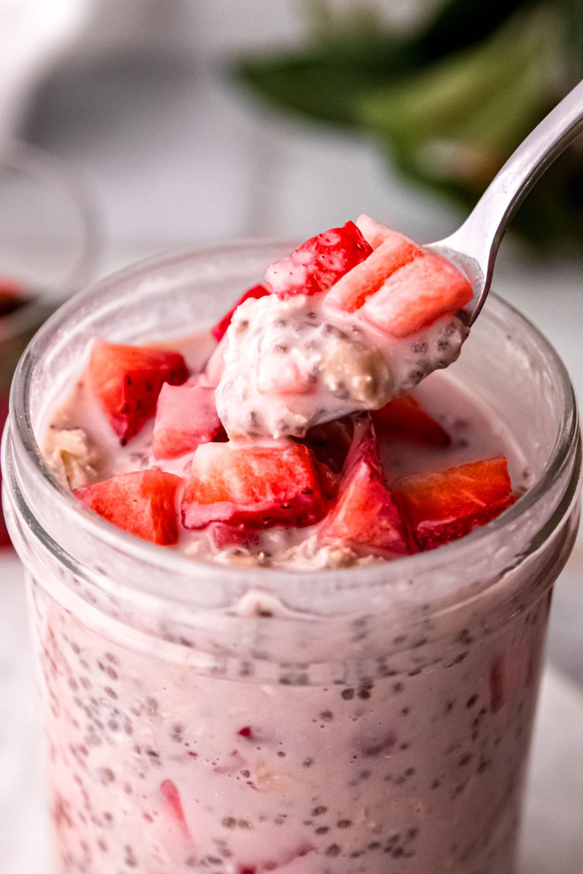 silver spoon dipping into a mason jar of high protein strawberry overnight oats topped with chopped fresh strawberries.