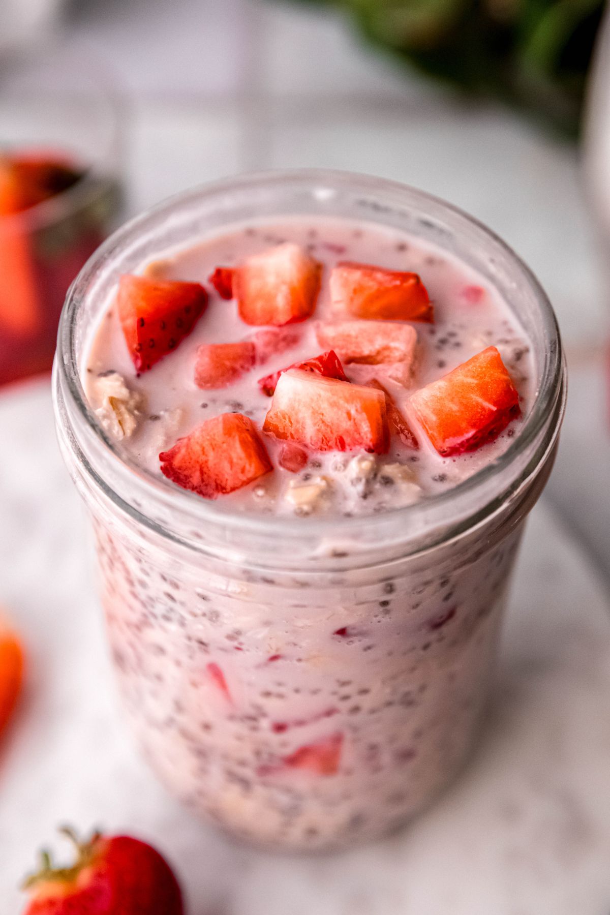 closeup overhead shot of a jar of pale pink strawberry protein oats topped with bright red fresh strawberries.