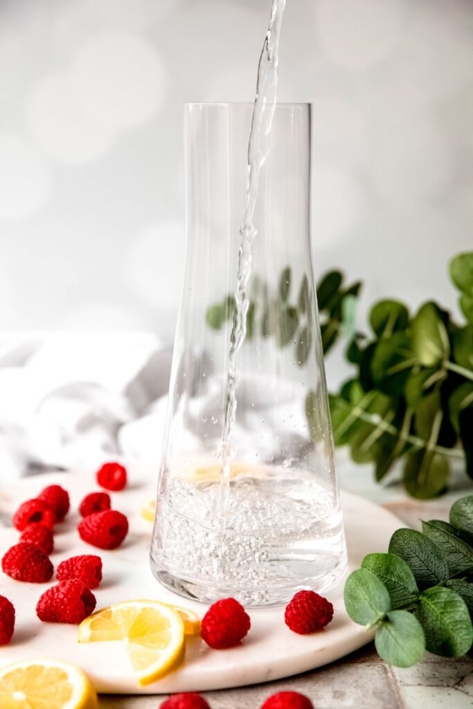 action shot of water being poured into a tapered glass pitcher.