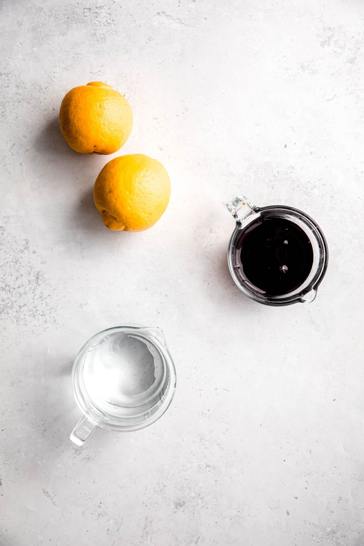 fresh lemons, blueberry syrup, and water measured out for making blueberry lemonade.
