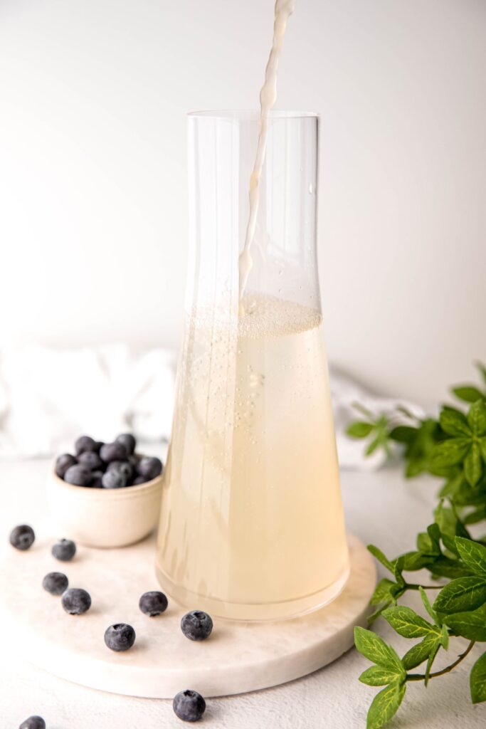 action shot of fresh lemon juice being added to the pitcher with the water.