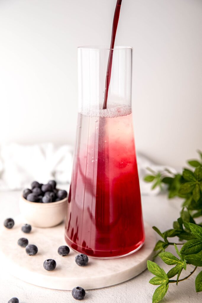 action shot of the unsweetened lemonade getting sweetened with a pour of blueberry simple syrup.
