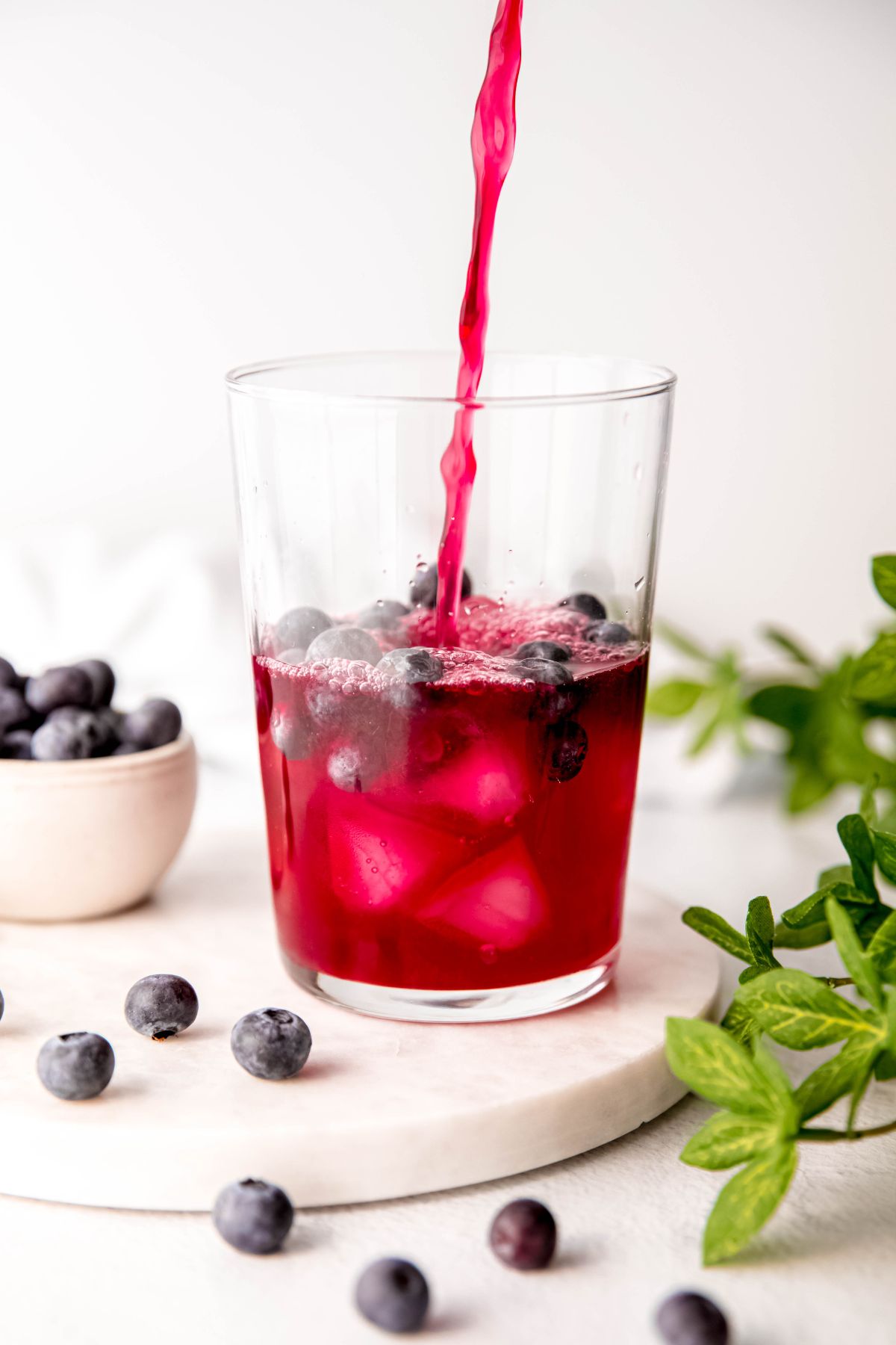 blueberry lemonade being poured into a glass of ice with fresh whole blueberries.